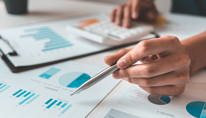 Table filled with paper with graphs and pie charts on as someone uses a calculator