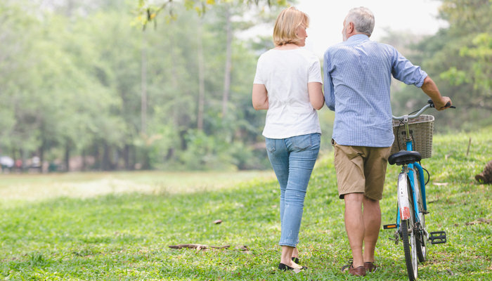 Senior couple walking through the park and pushing a bike