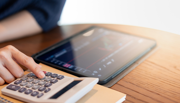 A person using a calculator while looking at a graph on a tablet.