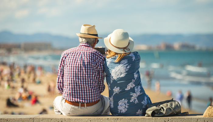 An older couple sitting on a wall at a beach.