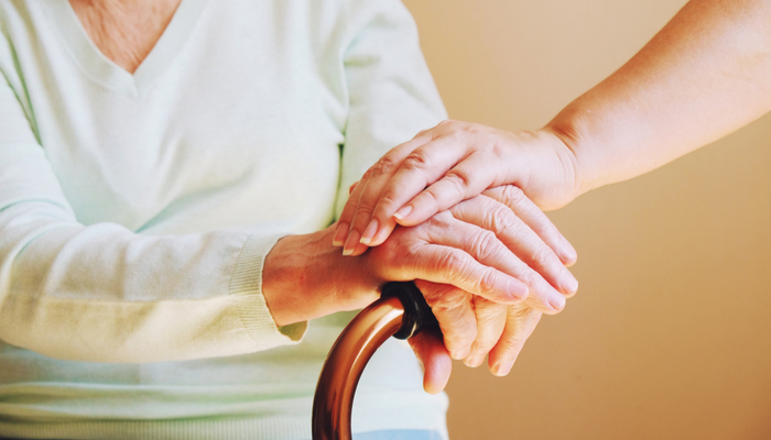 Close-up of someone holding hand the hand of an older woman with a walking aid.