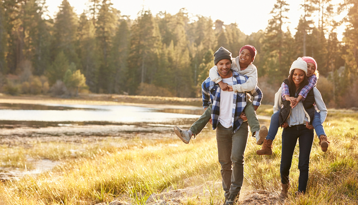 Parents walking through a park giving children a piggyback ride.