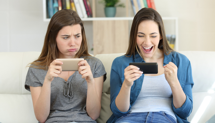 one girl looking envious at the delighted girl next to her on the sofa