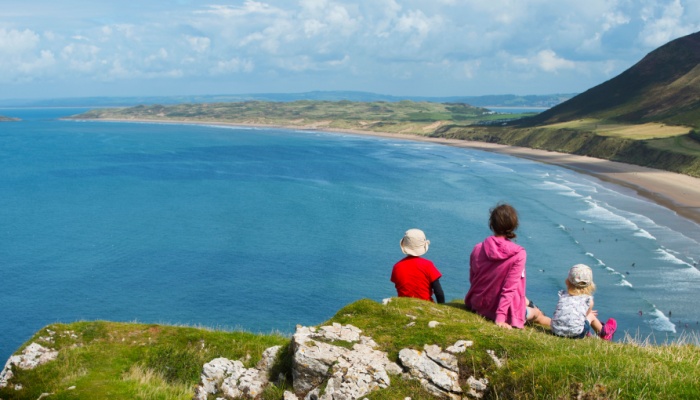 A family sitting on a clifftop overlooking a beach.