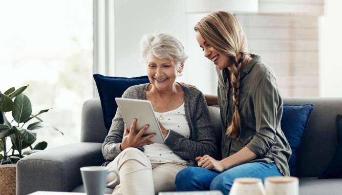 A woman showing her adult daughter something on a tablet.