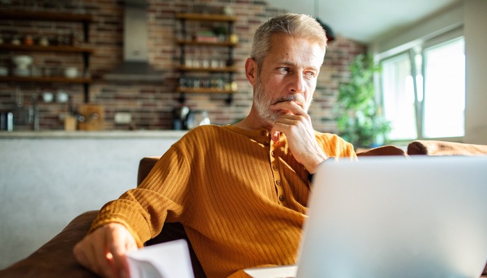 A man in his 50s thinking while using a laptop